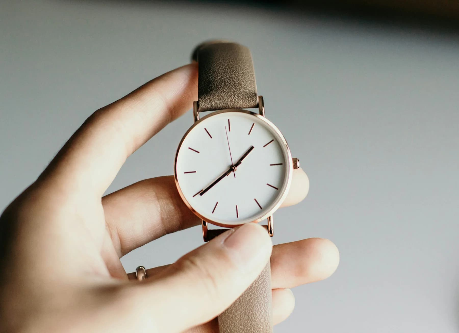Hand holding a minimalist watch with a white dial and tan strap