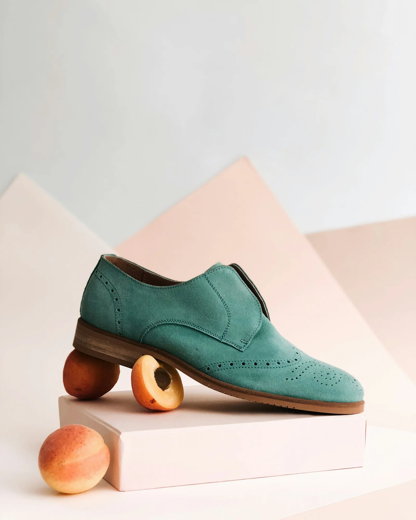 Teal suede loafer displayed on a pink geometric background